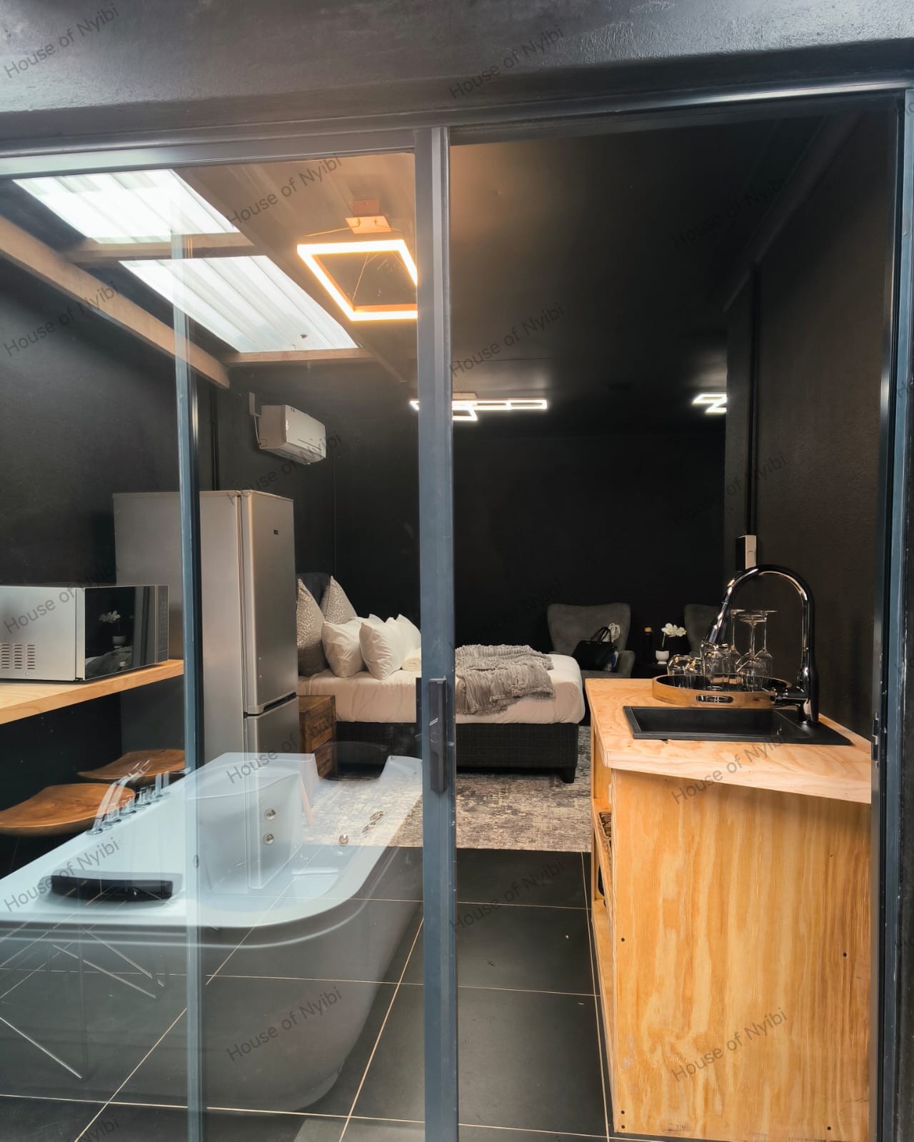 Zululami — glass-door view into the private room with kitchenette, bed and hot tub